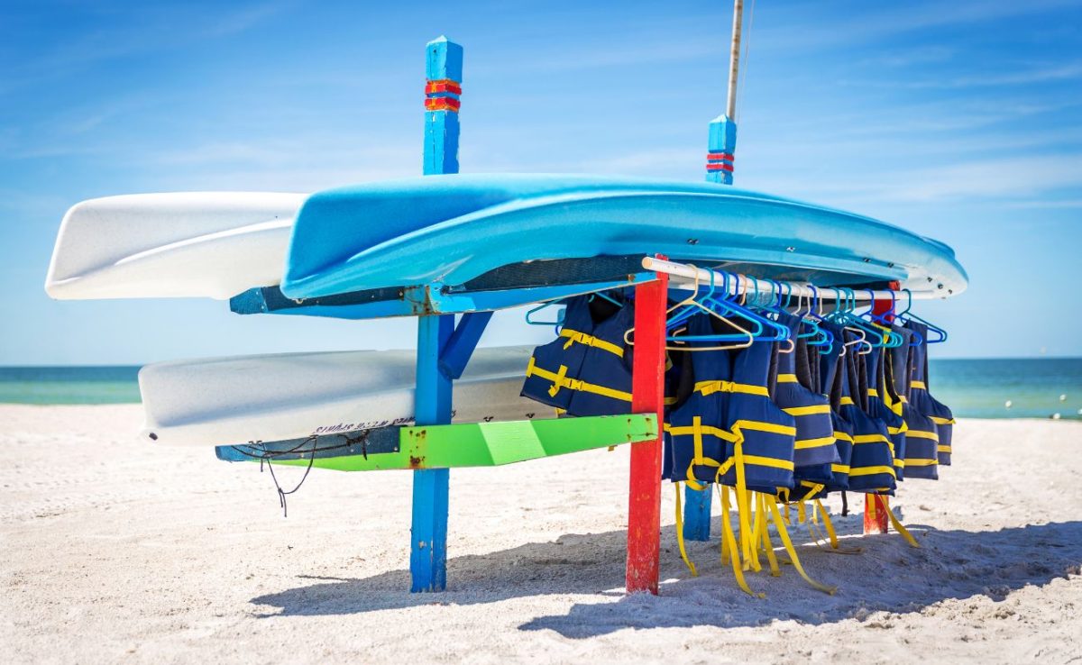 Bright blue and red ocean kayaks stacked on a rack along a sandy beach.