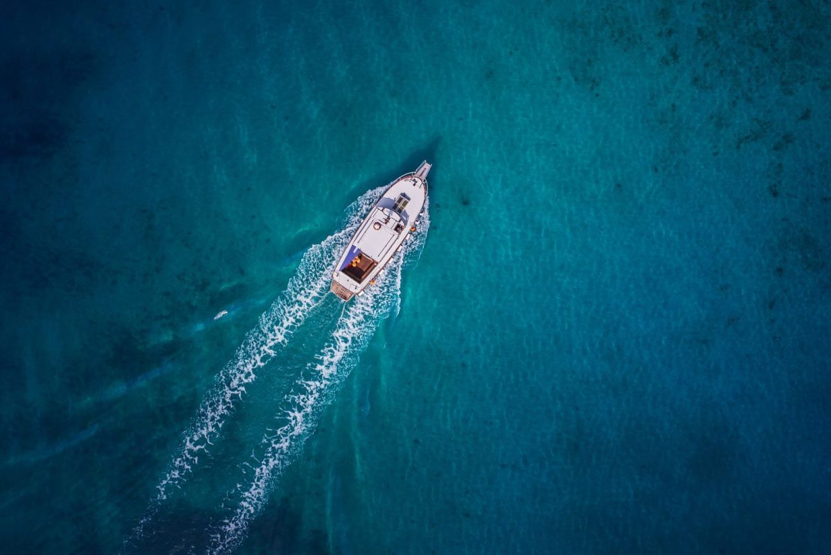 Aerial shot of a small white motorboat cruising through deep blue ocean water.