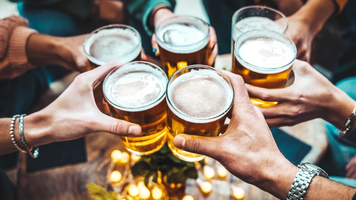 Friends holding up glasses of cold draft beer in a toast at an outdoor bar.