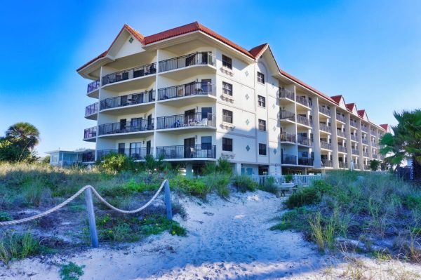 Front exterior of a white multi-story resort building set against a blue sky.