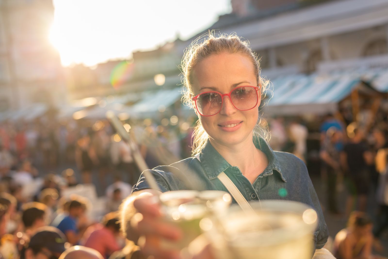A smiling woman wearing sunglasses and a denim jacket outdoors.