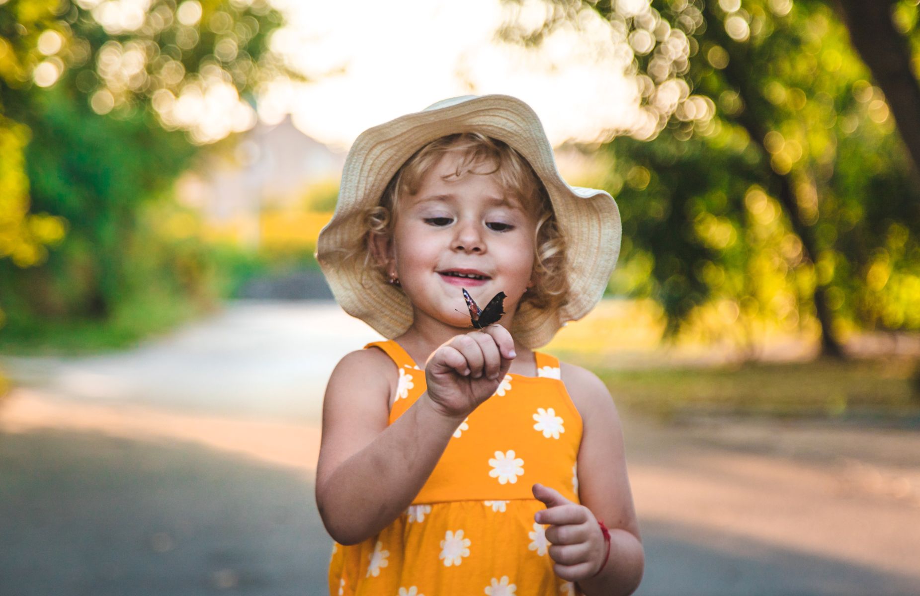 A young girl wearing a sun hat smiling in an outdoor setting.