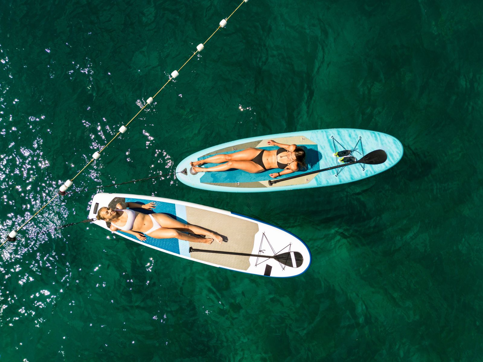 Aerial view of two people paddleboarding in turquoise ocean water.