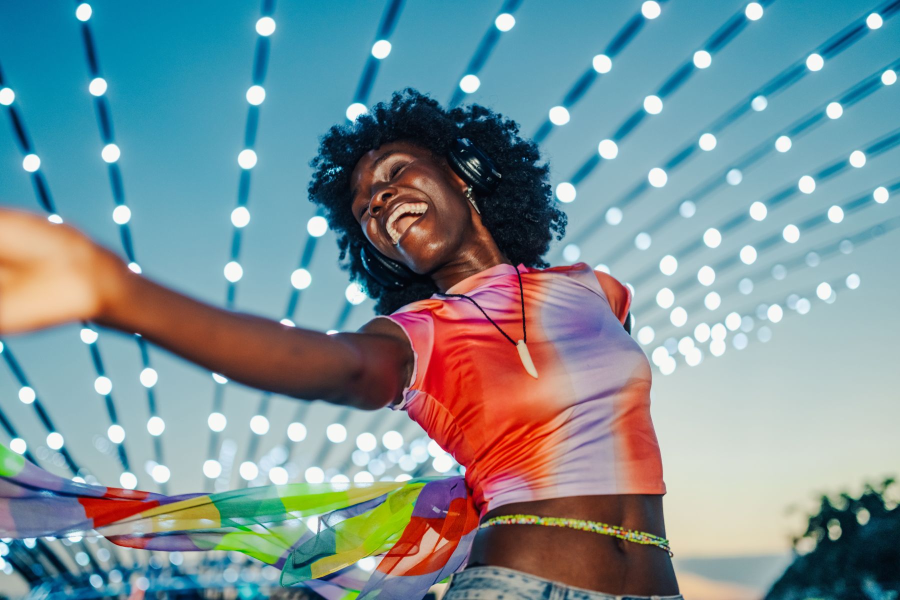 A smiling woman looking up near string lights outdoors at night.